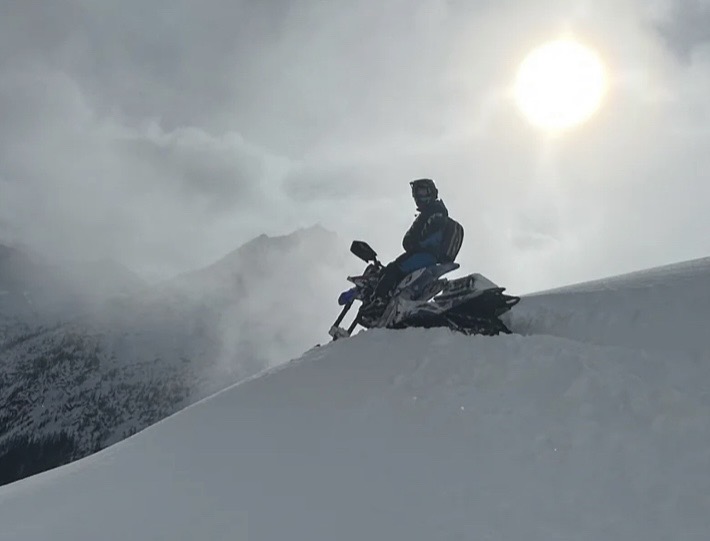 Rider carving through deep powder on a snowbike at sunrise